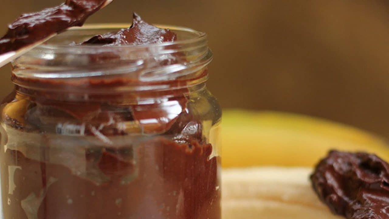 Nutella de aguacate y chocolate sin azúcar en un frasco de cristal con cuchillo untado
